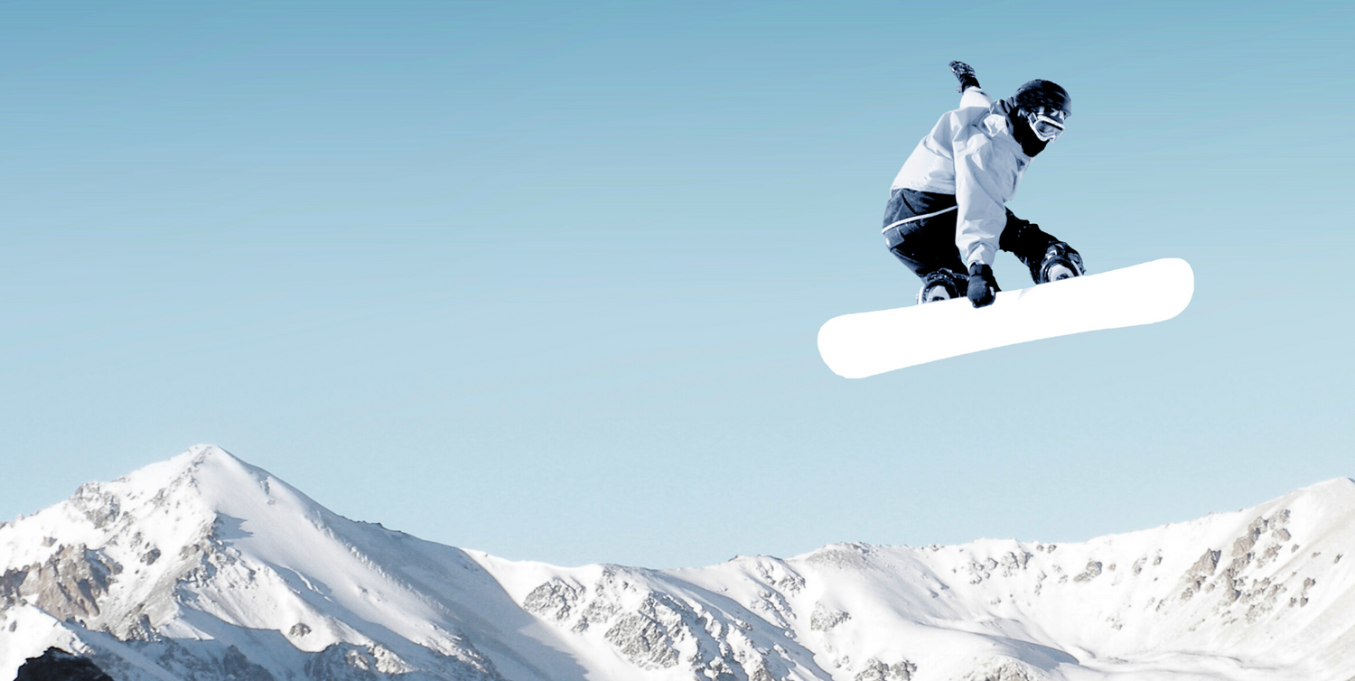 A snowboarder catches air while jumping off a snowy slope with breathtaking mountain peaks in the background
