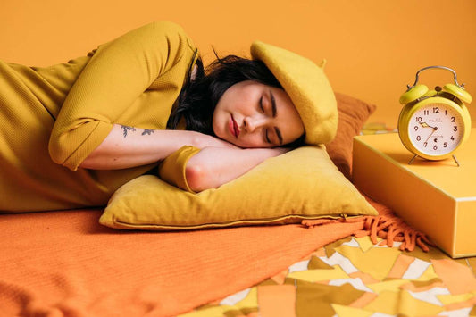 Woman in soft pajamas sitting up in bed at night, lit by a warm bedside lamp, reading a book with a Soothe Organic Sleep gummy bottle on the nightstand.